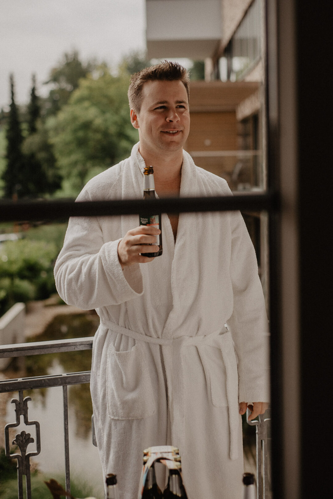 Mann im Bademantel trinkt Bier auf dem Hotelbalkon