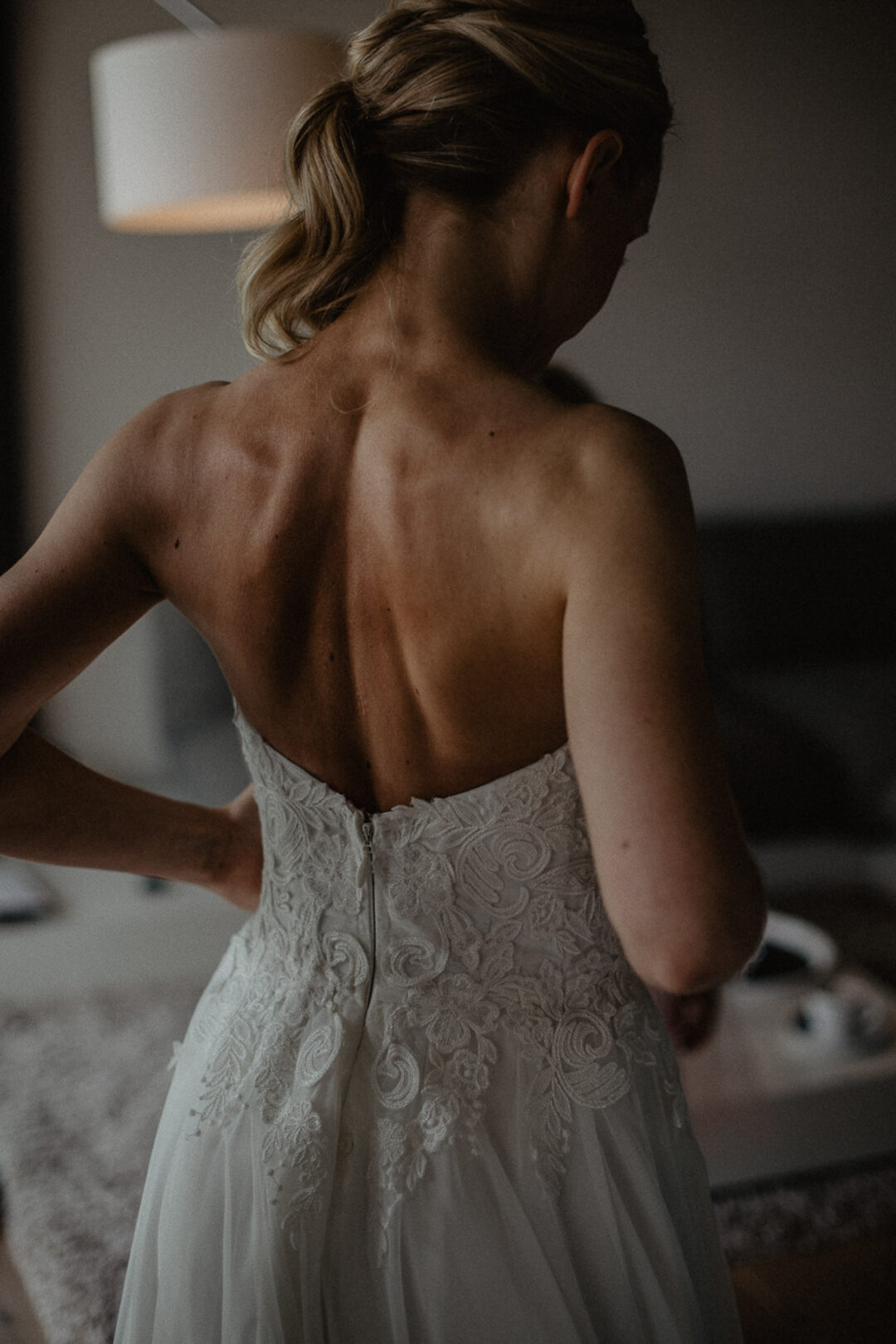Rückenansicht der Braut im Spitzenkleid beim Getting Ready