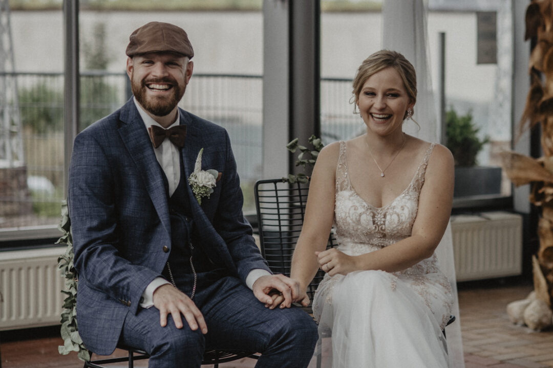 Brautpaar sitzt Hand in Hand und strahlt – pure Freude nach dem Ja-Wort