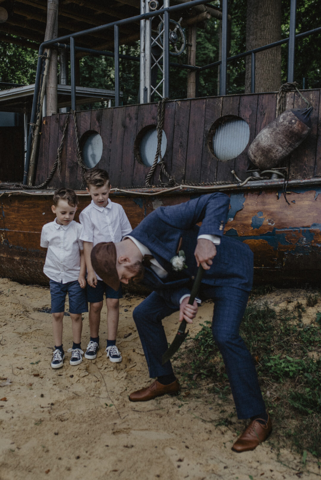 Bräutigam vergräbt etwas im Sand vor zwei Jungs