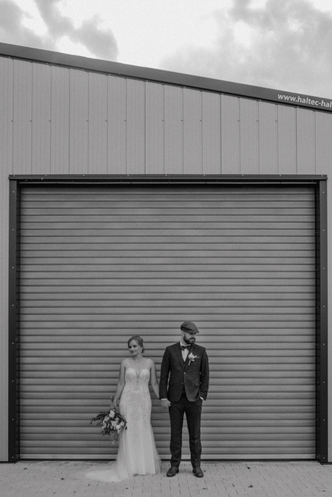 Brautpaar steht vor einem großen Industrietor für ihr Shooting
