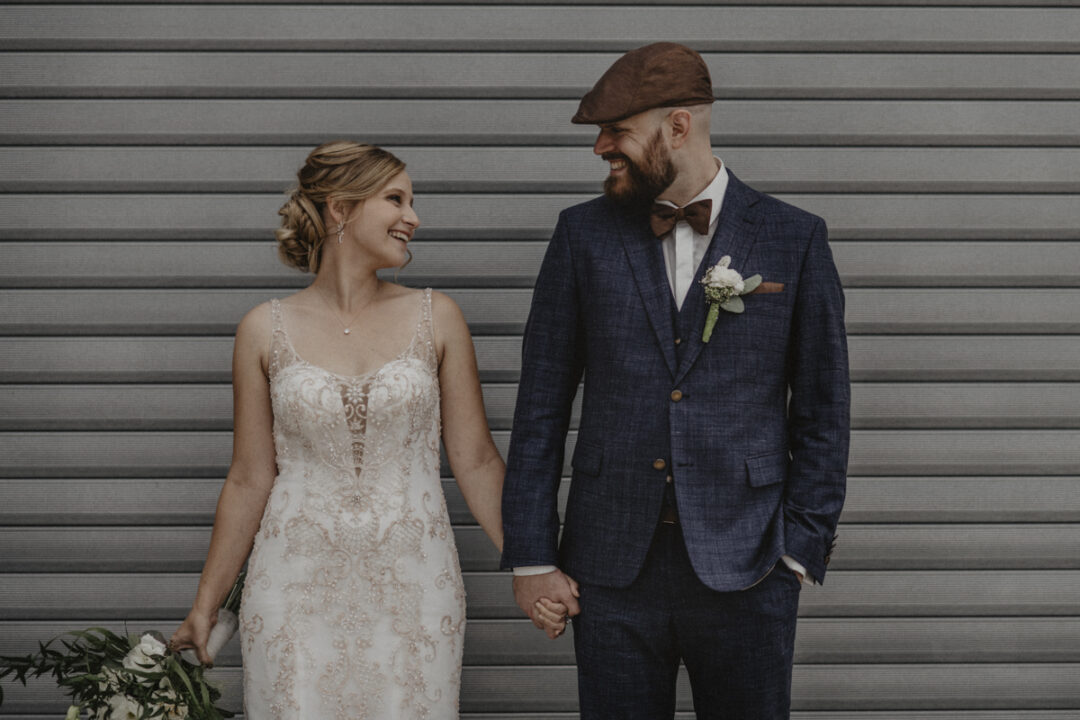 Brautpaar steht Hand in Hand vor grauem Metalltor