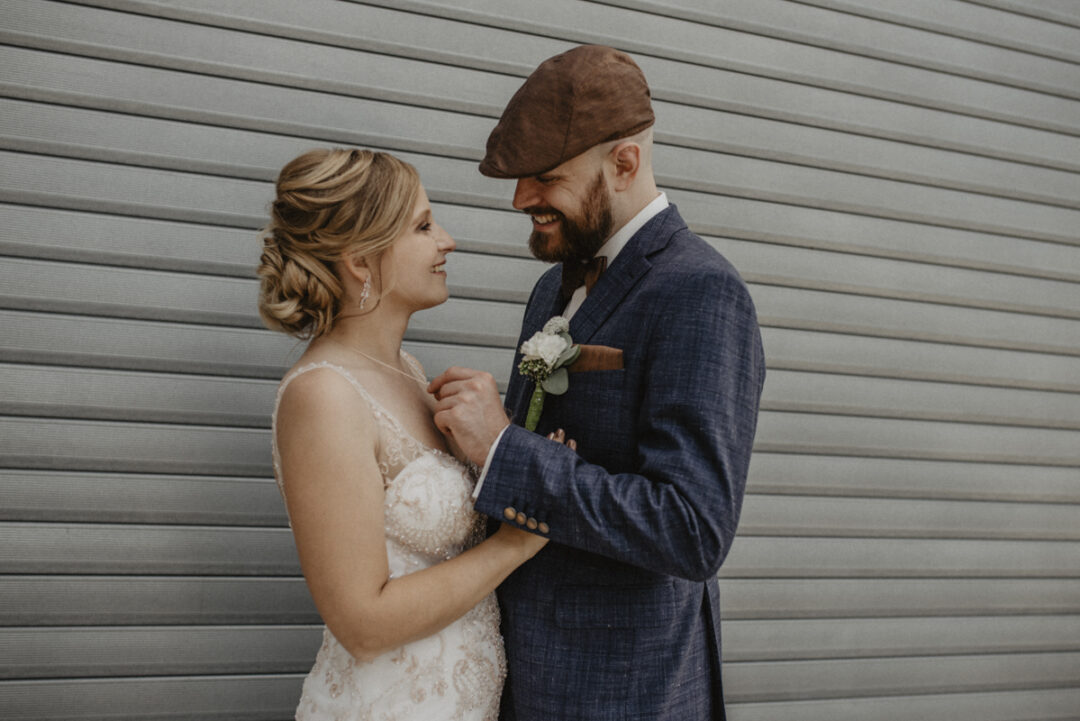 Braut und Bräutigam lachen sich verliebt an vor grauem Industrietor