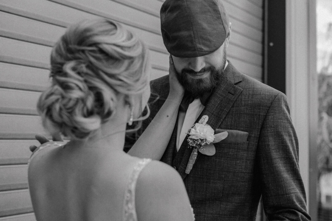 Rückansicht der Braut, wie sie dem Bräutigam zärtlich übers Gesicht streicht