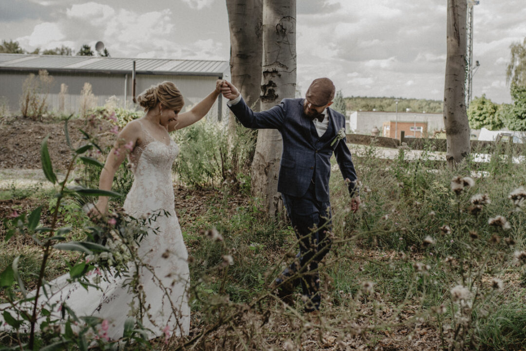 Brautpaar spaziert Hand in Hand durch wild gewachsene Natur