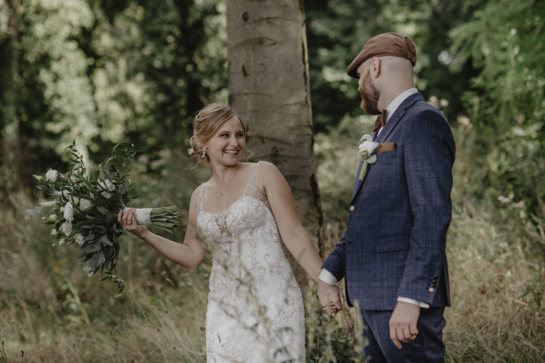 Braut schwingt ihren Strauß, während sie mit dem Bräutigam Händchen hält