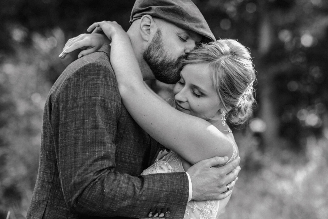 Bräutigam küsst Stirn der Braut – inniger Moment in Schwarz-Weiß