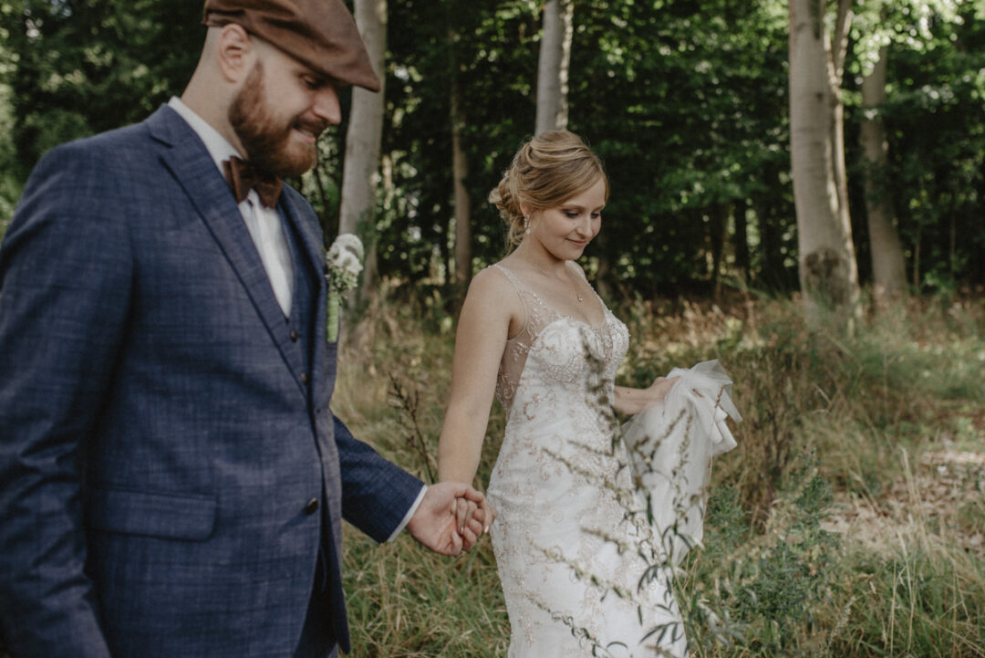 Braut und Bräutigam spazieren Hand in Hand durch die Natur