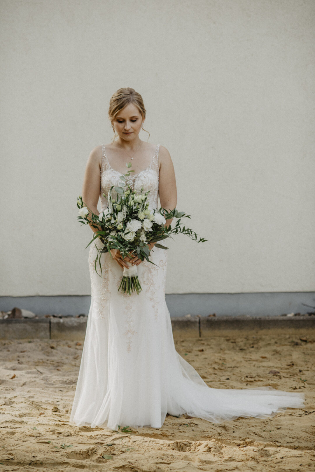 Braut in besticktem Kleid hält einen großen, grünen Brautstrauß und schaut liebevoll darauf