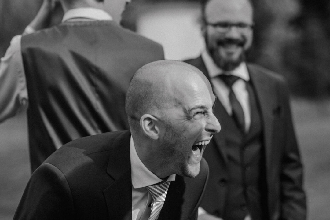 Schwarz-weiß-Aufnahme eines lachenden Gastes im Anzug während einer Unterhaltung