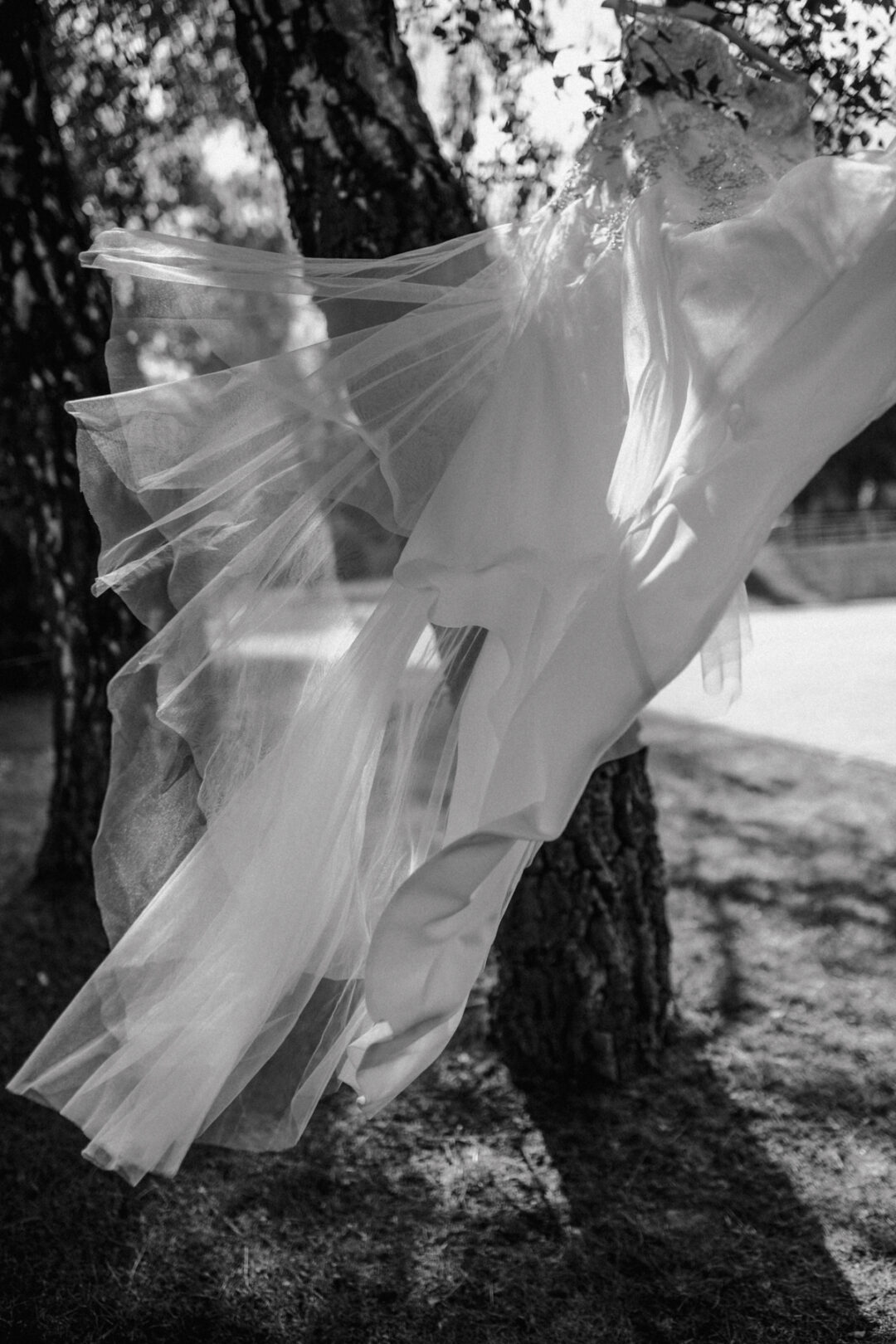 Leicht und elegant – das Hochzeitskleid als Highlight vor der Trauung Brautkleid weht im Wind – Detailaufnahme vor rustikalem Baum im industriellen Ambiente