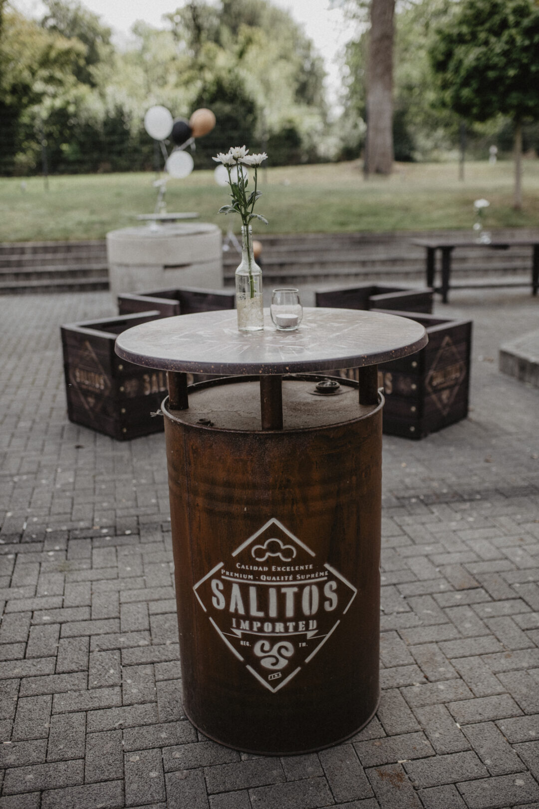 Stehtisch aus Ölfass mit Salitos-Aufdruck und Blumendeko – moderne Hochzeit