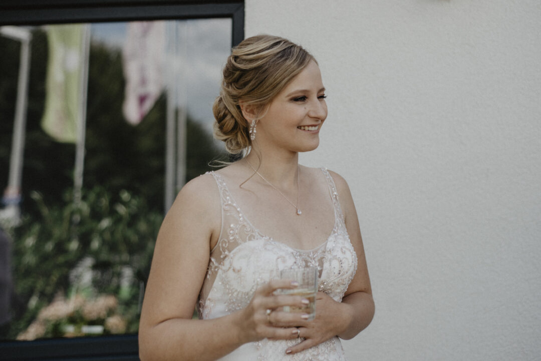 Porträt der strahlenden Braut mit Sektglas – Glückliche Momente vor der Trauung