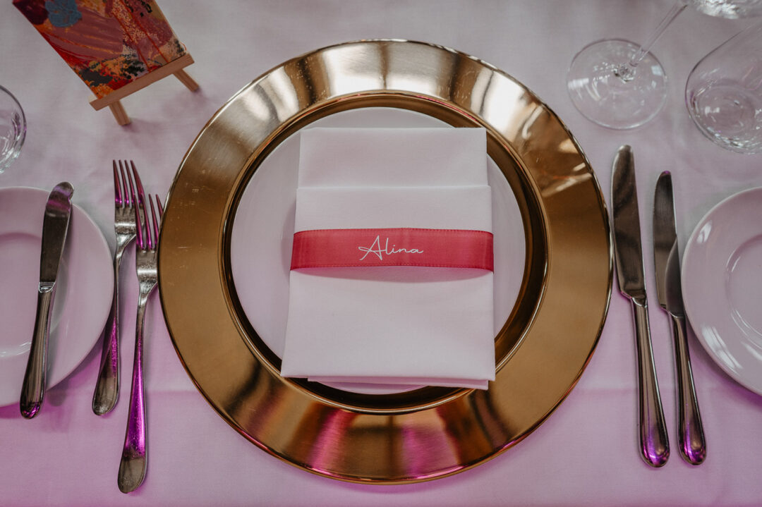 Goldene Platzteller mit pinker Namensbanderole zur Hochzeit