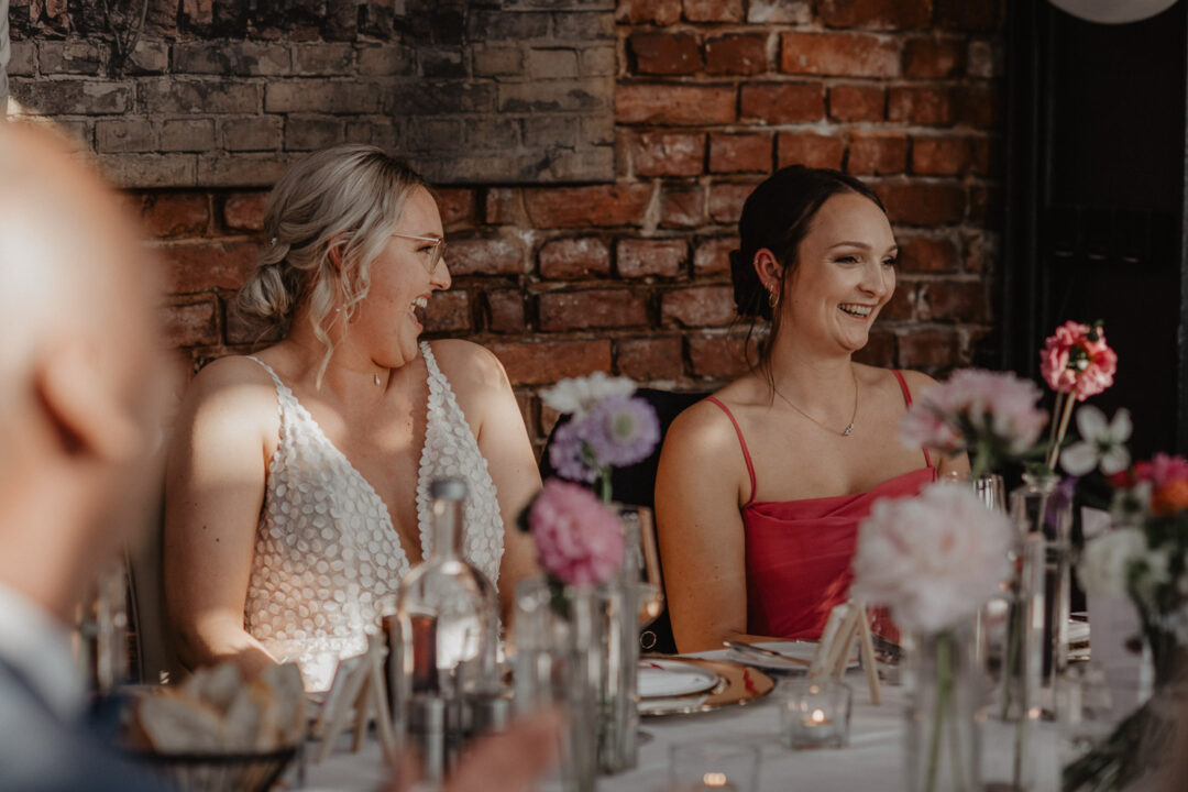 Braut und Trauzeugin lachen laut während der Feier