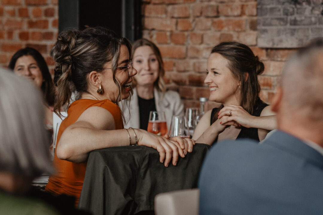 Freundinnen lachen gemeinsam während der Hochzeitsrede