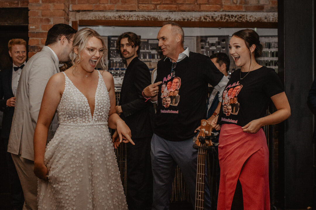 Braut lacht über Gäste mit bedruckten T-Shirts bei der Hochzeit