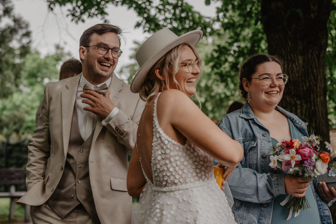 Brautpaar lacht gemeinsam mit Hochzeitsgästen im Grünen