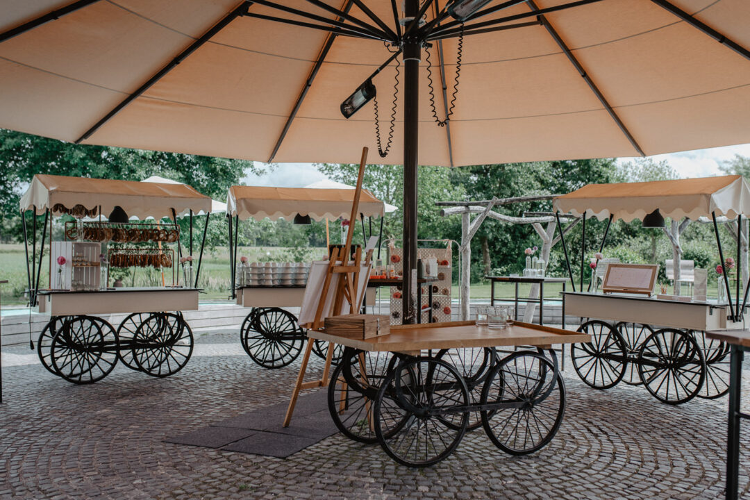 Hochzeitslocation mit Marktständen unter großem Sonnenschirm