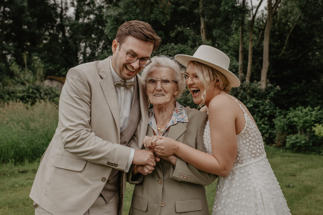 Brautpaar lacht mit Oma im Garten des Beverland