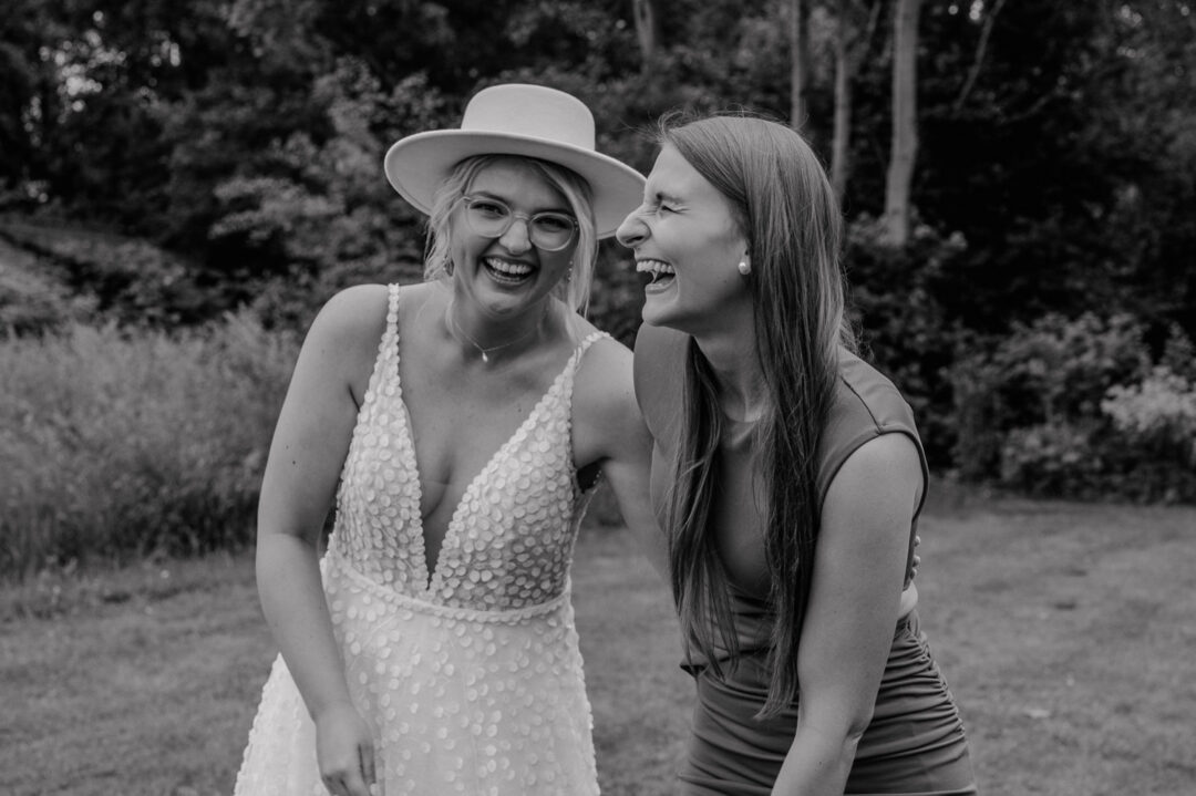Braut lacht herzlich mit Freundin auf der Wiese