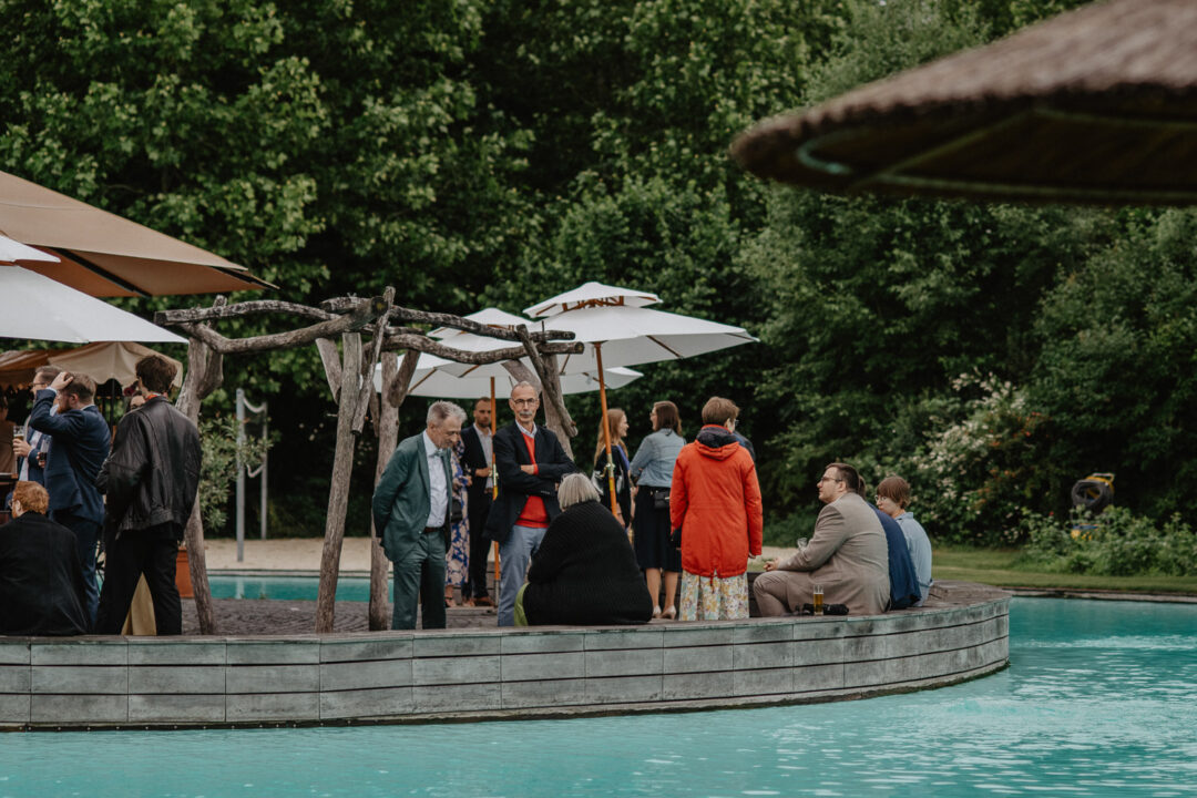 Hochzeitsgäste stehen auf Insel im Pool unter Schirmen