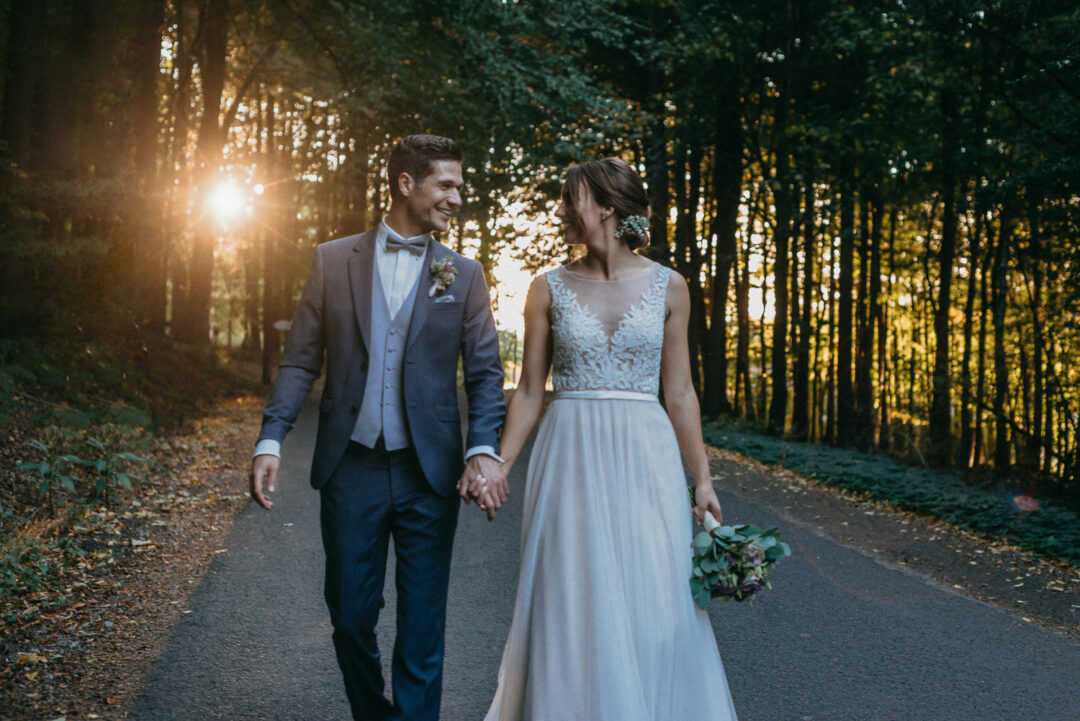 Brautpaar geht Hand in Hand auf der Allee in der Abendsonne.