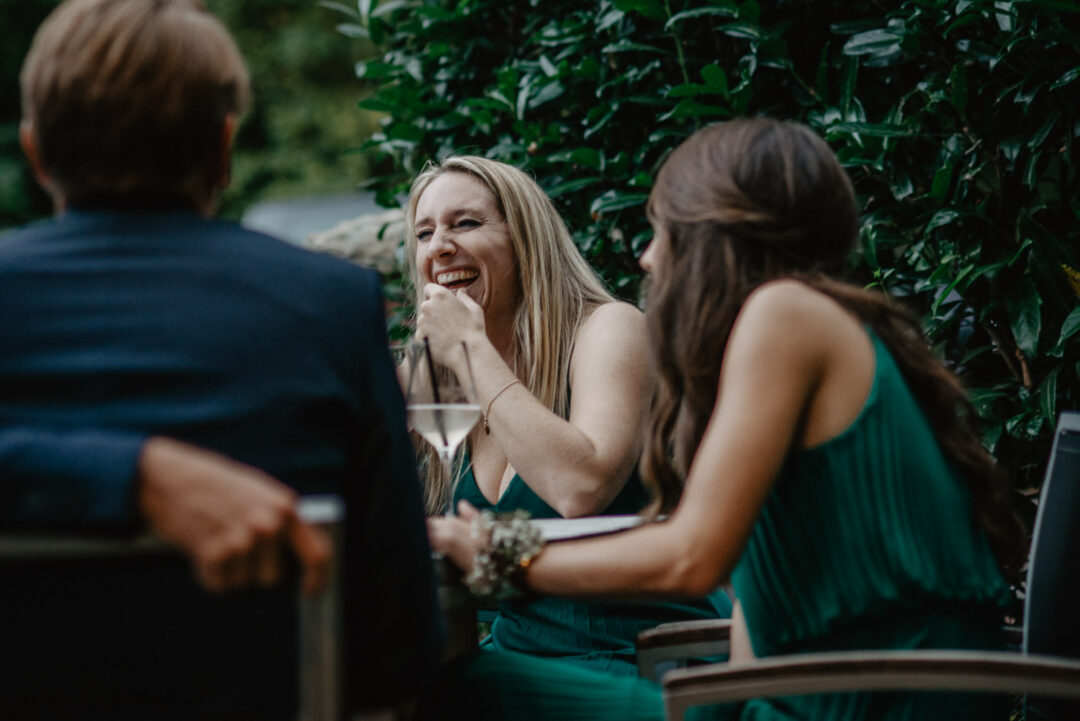 Junge Frau lacht herzlich mit Freunden beim Empfang im Garten.