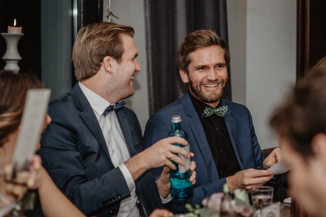 Zwei männliche Gäste lachen bei Tisch während der Feier.