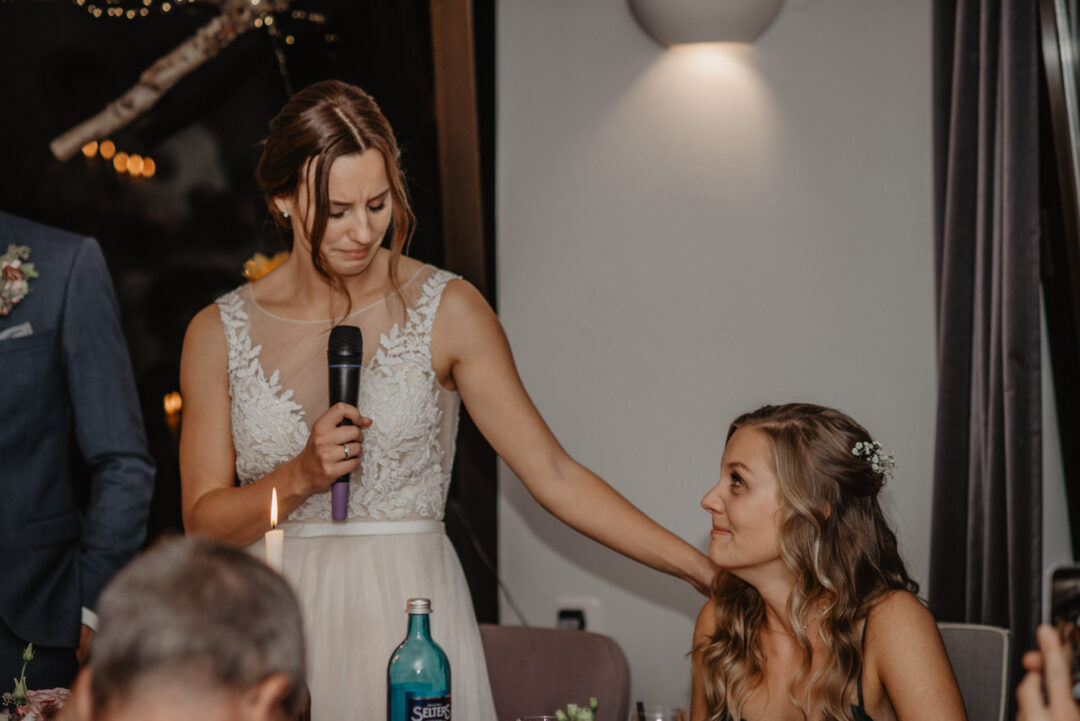 Braut hält eine emotionale Rede und legt die Hand auf die Schulter einer Freundin.