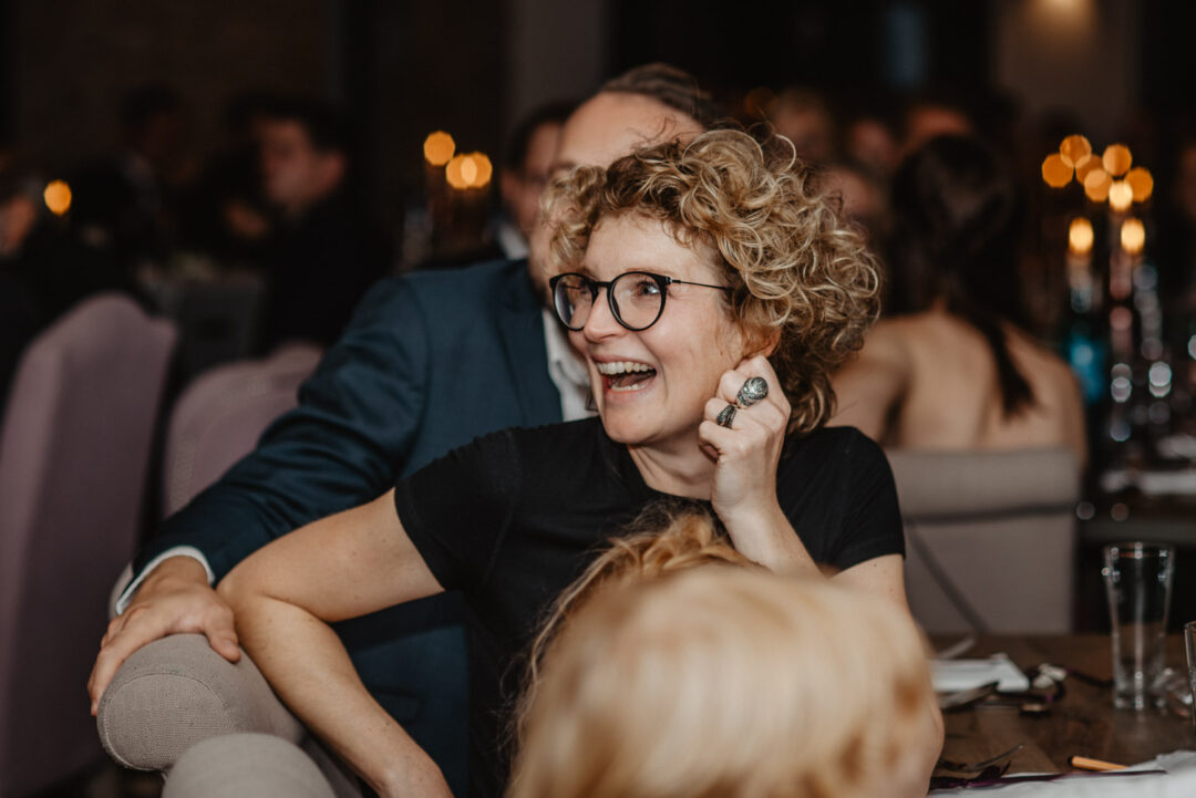 Frau mit lockigem Haar lacht während der Hochzeitsrede.