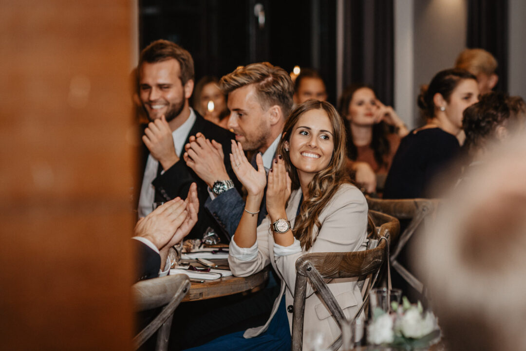Gäste klatschen und lächeln während einer Rede im Saal.