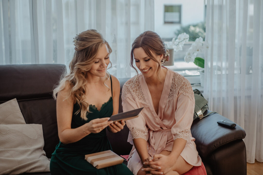 Braut und Brautjungfer sitzen zusammen und öffnen ein Geschenk.