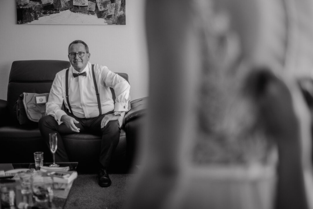 Vater sitzt auf dem Sofa und betrachtet seine Tochter im Brautkleid, Schwarz-Weiß.