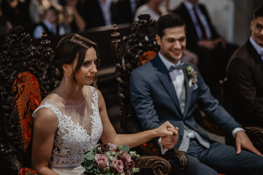 Braut und Bräutigam sitzen nebeneinander und halten sich die Hände.