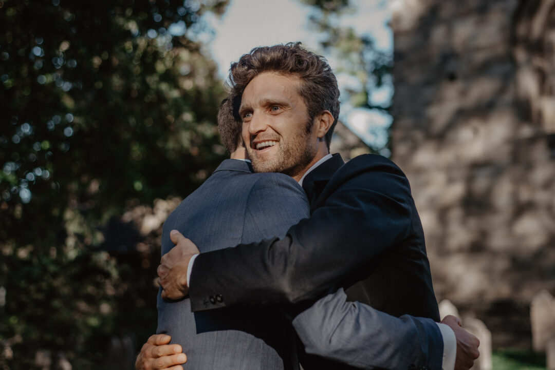 Bräutigam umarmt einen Freund herzlich nach der kirchlichen Trauung.