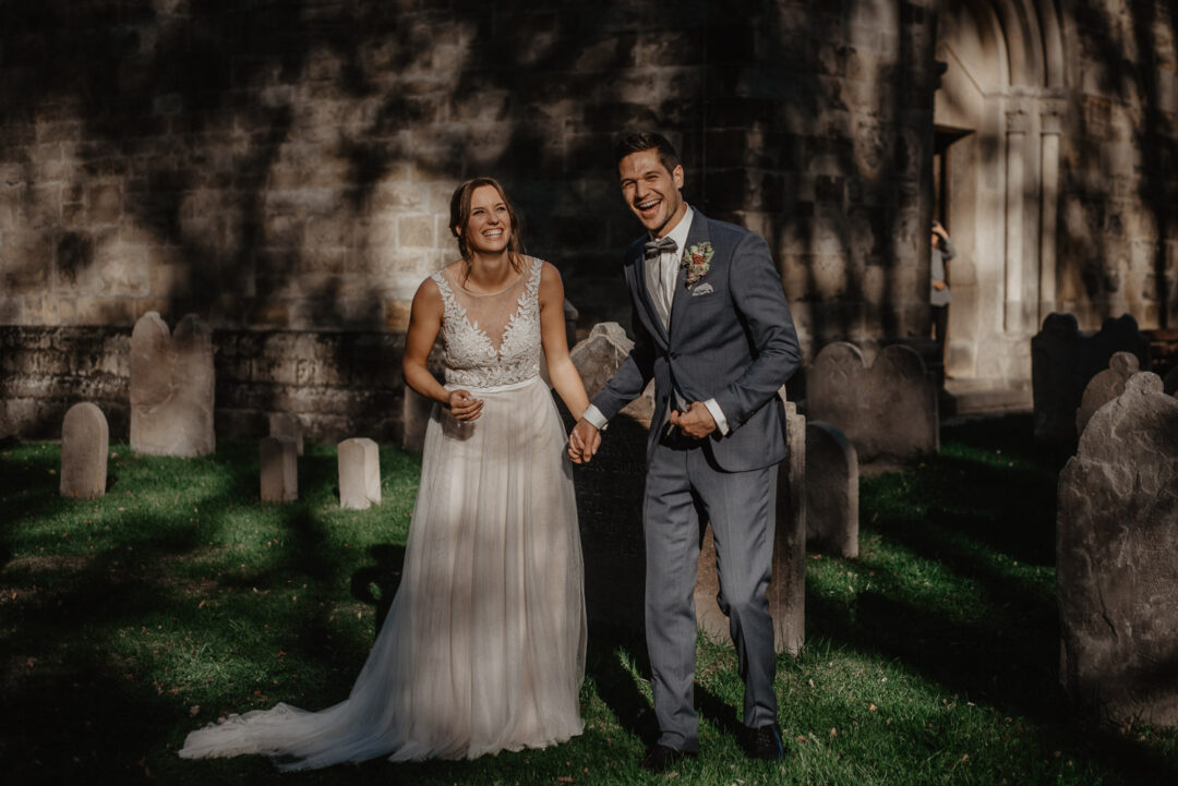 Brautpaar steht lachend zusammen im Kirchgarten nach der Trauung.