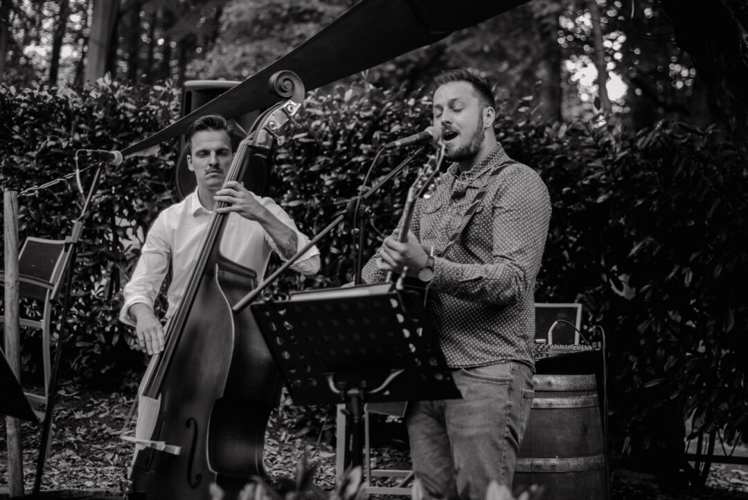 Zwei Musiker mit Kontrabass und Gitarre spielen live im Freien, Schwarz-Weiß.