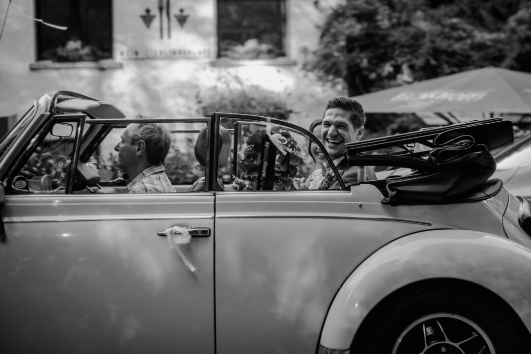 Braut und Bräutigam fahren lachend in einem Cabrio, Schwarz-Weiß.
