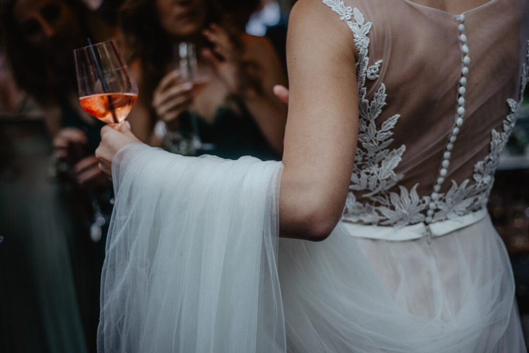 Braut hält ein Glas Aperitif in der Hand beim Empfang vor dem Wirtshaus.