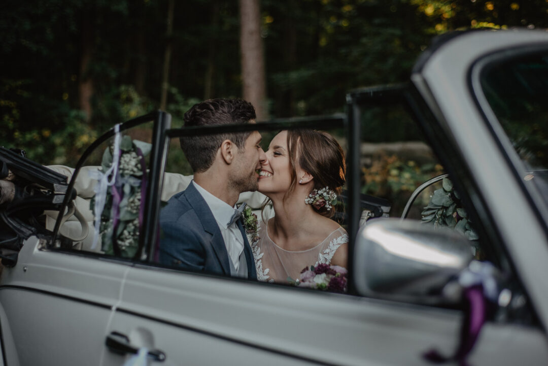 Braut und Bräutigam küssen sich im Cabrio während der Herbsthochzeit.