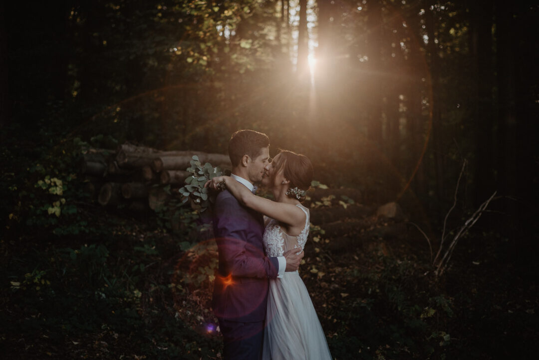 Brautpaar umarmt sich eng im Wald bei Sonnenuntergang.