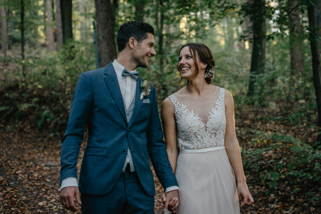 Braut und Bräutigam lachen sich auf dem Waldweg herzlich an.