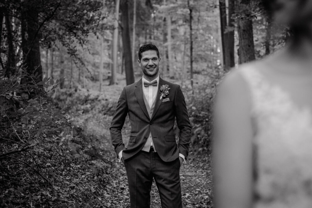 Bräutigam lächelt in die Kamera, Schwarz-Weiß Portrait im Wald.