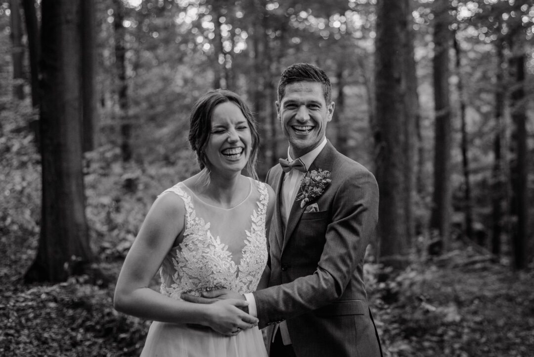 Brautpaar lacht laut bei einer Umarmung im Wald, Schwarz-Weiß.