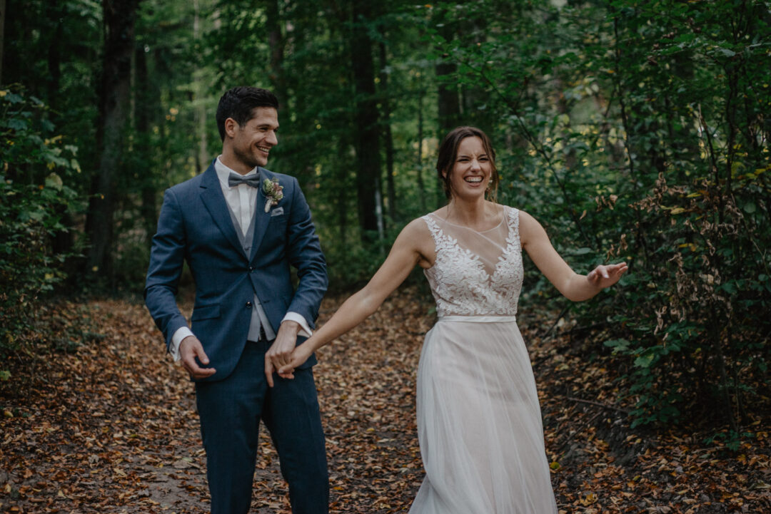 Braut und Bräutigam lachen gemeinsam während des Shootings im Wald.