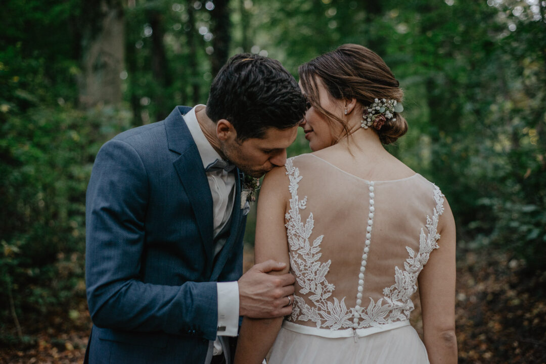 Bräutigam küsst die Schulter der Braut im Wald.