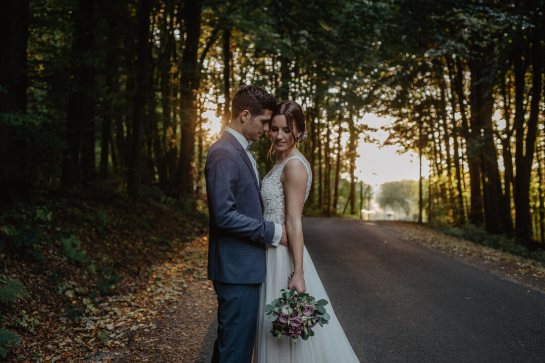 Brautpaar steht eng umschlungen auf der Allee im Abendlicht.